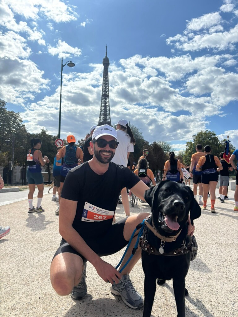 Arthur accroupi en tenue de course avec Unny debout à ses côtés avec en fond la Tour Eiffel sur un ciel bleu